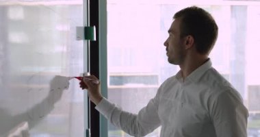 Odaklanmış işadamı elindeki işaretle ofisteki beyaz tahtaya notlar yazıyor.