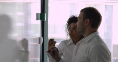 Ciddi Afrikalı ve Kafkasyalı iş arkadaşları birlikte çalışarak beyaz tahtaya resim çiziyorlar.