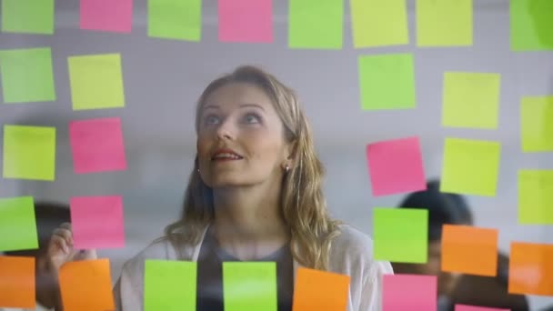 Mladá podnikatelka nahrazující lepicí poznámky na plánování skleněné tabule — Stock video