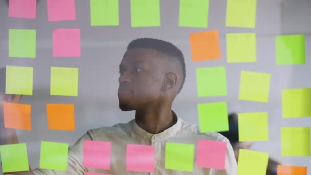 Afrikaanse student werknemer schrijven vervangen plakkerige notities op scrum board — Stockvideo