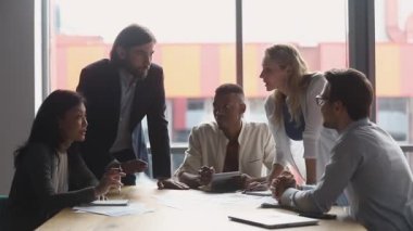 Çok ırklı beyin fırtınası ekibi ofis masasında gülüşmeler hakkında konuşuyor.