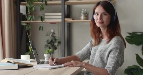 Kvinna sitter vid skrivbordet och lär sig språk leende tittar på kameran — Stockvideo