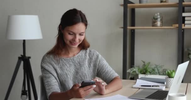 Женщина отвлекается от работы в чате с другом, используя смартфон — стоковое видео