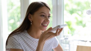 Gülümseyen genç kadın cep telefonunda dijital ses asistanı kullanıyor