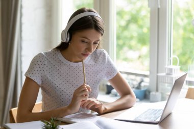 Kulaklıklı kız evde dizüstü bilgisayarla çalışıyor.