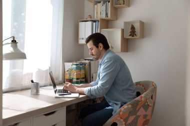 Odaklanmış beyaz adam evde dizüstü bilgisayarla çalışıyor.