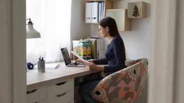 Odaklanmış milenyum kızı belgelerle dizüstü bilgisayarda çalışıyor.