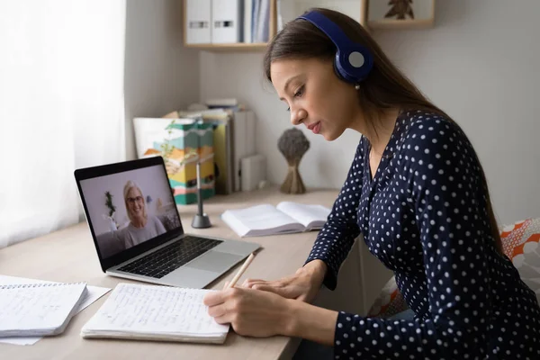 Kvinna i hörlurar gör anteckningar studerar på bärbar dator — Stockfoto