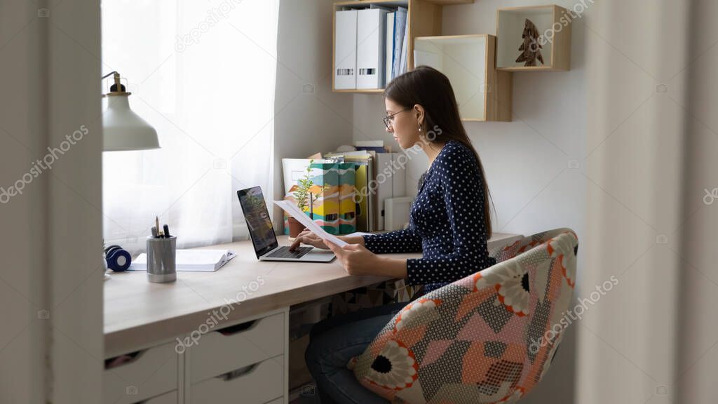 Focused millennial girl work on laptop with documents