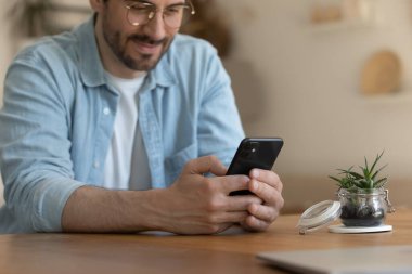 Genç adam modern akıllı telefon zımbırtıları kullanarak masada oturuyor.