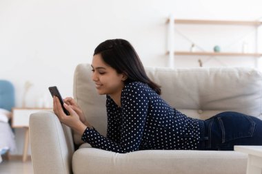 Mutlu Asyalı kız akıllı telefon kullanarak kanepede rahatla.