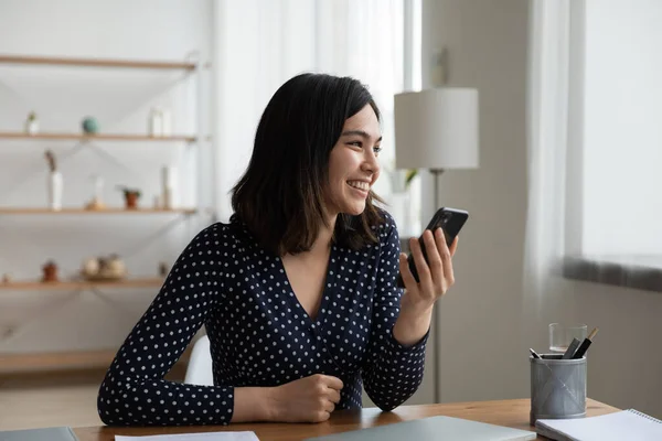 Sonriente chica asiática uso de teléfono celular soñando o pensando — Foto de Stock