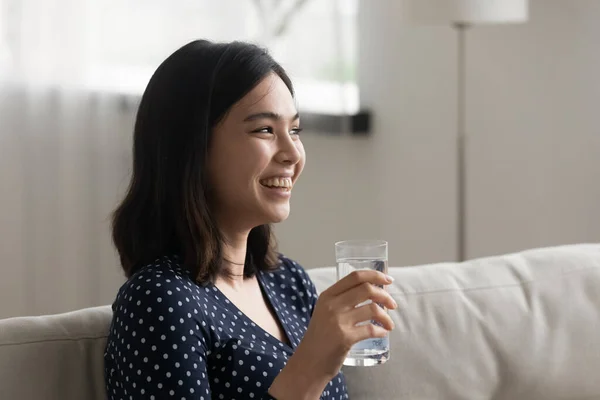 Smiling Asian girl drink clean mineral water form glass