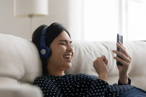 Overjoyed millennial Asian girl in headphones using smartphone — Stock Photo, Image