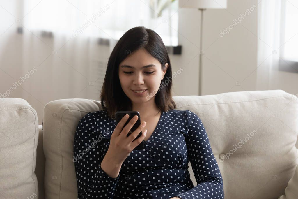 Millennial Vietnamese girl using cellphone relaxing at home