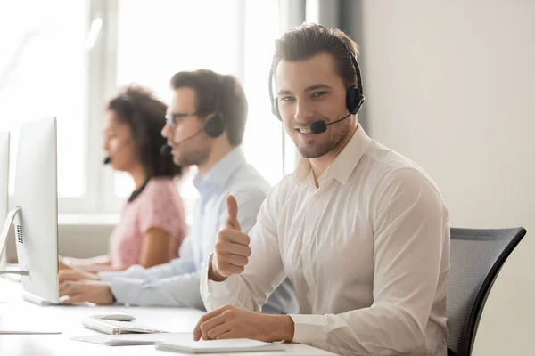 Smiling customer support service operator in headset showing thumbs up