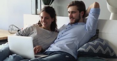 Mutlu genç çift yatakta dinleniyor, bilgisayardan bilgi alıyor..