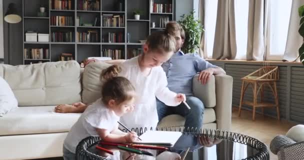 Lächelnde Eltern relaxen auf der Couch, während kleine Kinder zeichnen. — Stockvideo