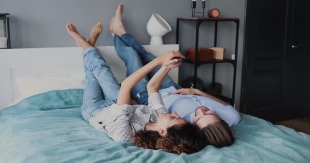 Aimer sourire couple familial couché sur un lit confortable, en utilisant un smartphone. — Video