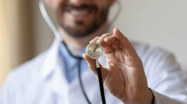 Odaklan. Elinde steteskop tutan gülümseyen genç bir kardiyolog..