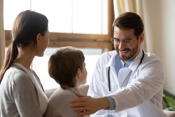 Emozionale giovane medico accarezzando spalla di bambino piccolo ragazzo in visita clinica. — Foto Stock