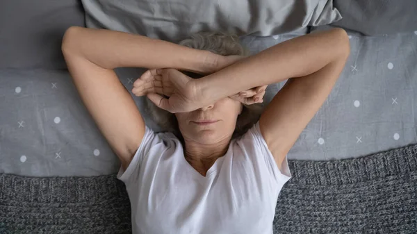 Top view aged woman lying on bed suffers from insomnia