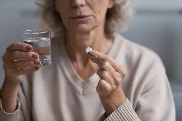 Closeup view senior woman holding glass of water and pill