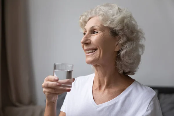 Femme âgée souriante tenant un verre d'eau plate — Photo