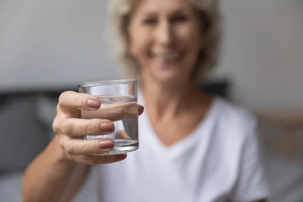 Äldre kvinna sträcka arm till kamera med glas vatten — Stockfoto