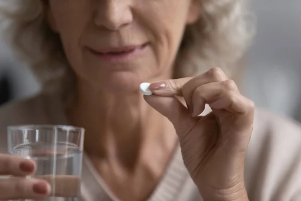 Elderly woman holding pill and glass of water closeup image — Stock Photo, Image