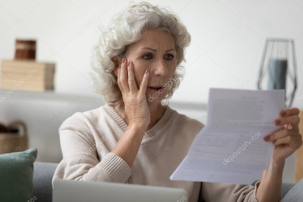 Senior woman reading letter feels disappointed having financial problems