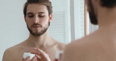 Yakışıklı genç adam nemlendirici yüz kremi sürüyor..