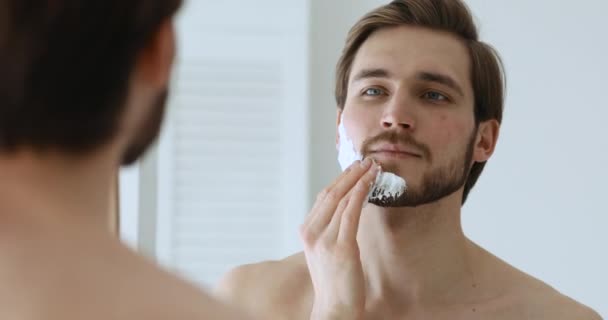 Snygg kille som använder mousse för ansiktshårborttagning rutin. — Stockvideo