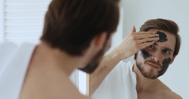 Hombre joven aplicando máscara de arcilla de carbón negro. — Vídeos de Stock