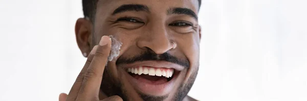 Nahaufnahme überglücklicher afroamerikanischer Mann, der feuchtigkeitsspendende Gesichtscreme aufträgt — Stockfoto