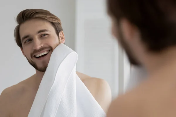 Reflexão espelho sorrindo jovem limpando rosto com toalha branca — Fotografia de Stock