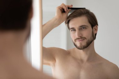 Aynadaki yansımayı kapat yakışıklı genç adam saçlarını tarıyor.