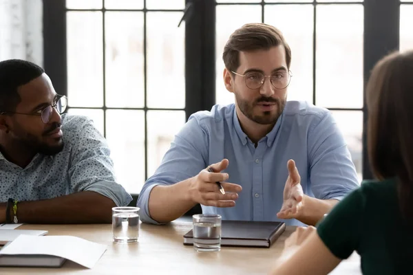 Confident young businessman wearing glasses speaking at corporate meeting