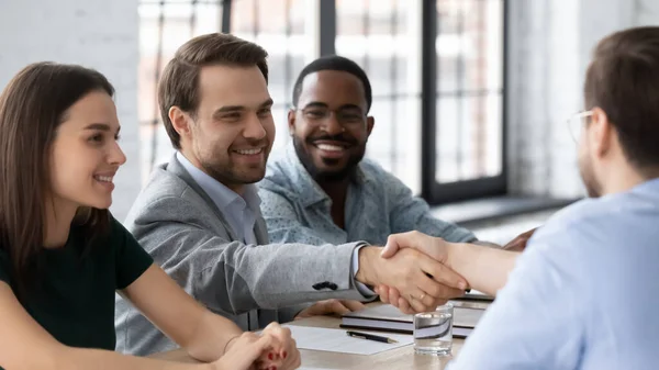 Gente de negocios sonriente dándose la mano, sentados a la mesa en la sala de juntas — Foto de Stock