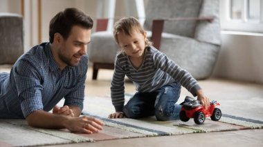 Gülümseyen genç baba, küçük çocukla en sevdiği oyuncak arabayı oynuyor..