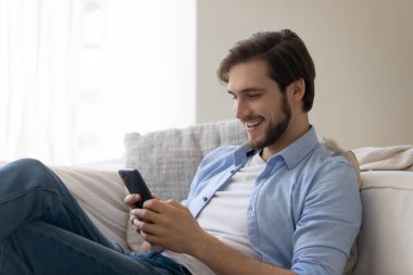 Gülümseyen neşeli genç adam akıllı telefon kullanıyor, internette sörf yapıyor, internette sohbet ediyor.