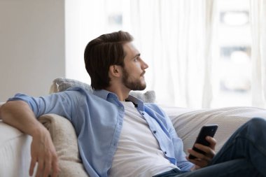 Hayalperest genç adam gevşiyor, akıllı telefon tutuyor, boş zamanların tadını çıkarıyor.