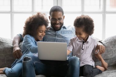 Mutlu çift ırklı babalar dizüstü bilgisayarda küçük çocuklarla video izler.