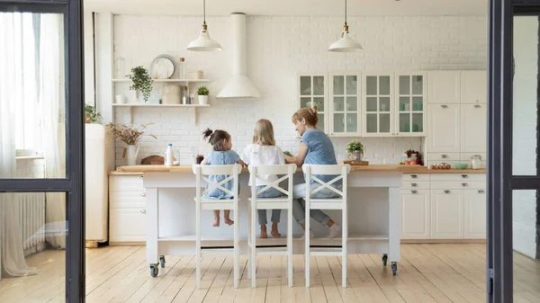 Rear view of mother and two little daughters cooking breakfast — Stock Photo, Image