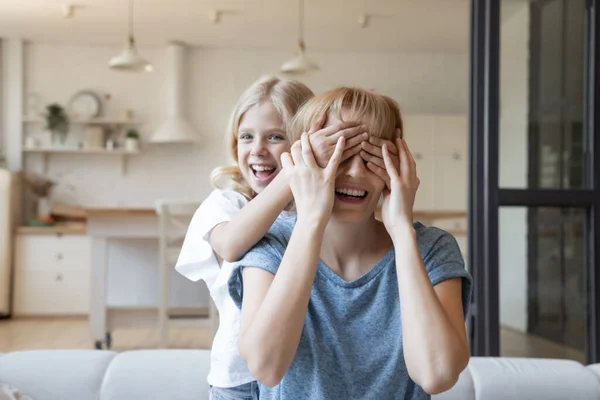 Непослушная маленькая девочка закрывает глаза смеющейся матери с ладонями — стоковое фото