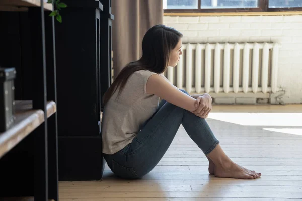 Zamyšlená depresivní mladá žena sedící na podlaze objímající kolena — Stock fotografie