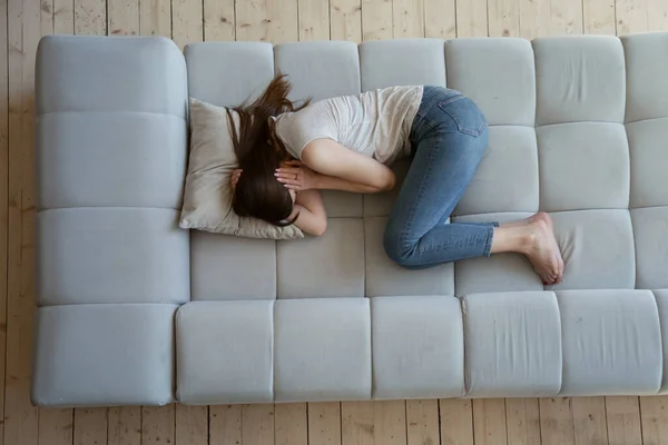 Distressed young female snuggling down on couch at home