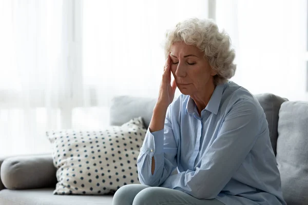Uitgeputte volwassen vrouw die last heeft van hoofdpijn binnen. — Stockfoto