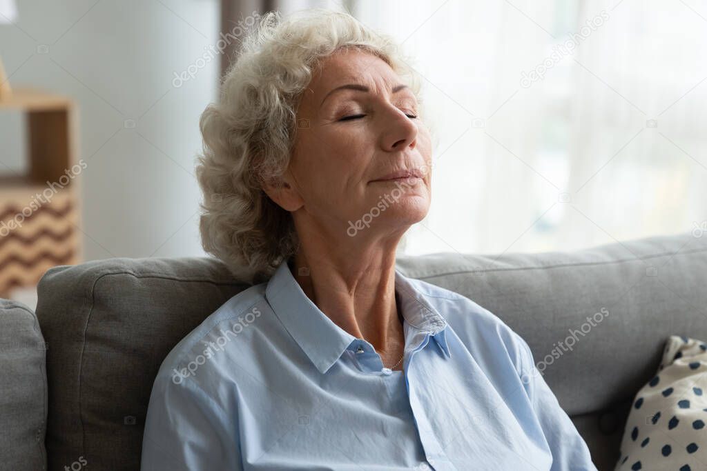 Tranquil middle aged senior female retiree relaxing on comfortable sofa.