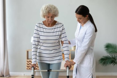 Sağlık çalışanı olgun engelli bir kadının çerçeveyle yürümesine yardım ediyor..